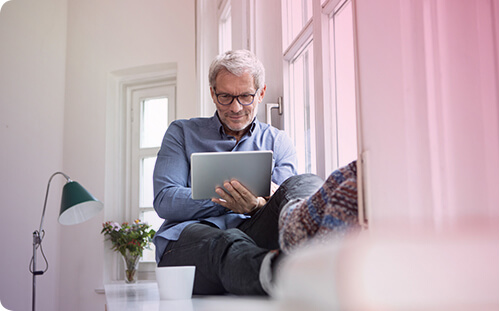 Mann sitzt mit Tablet neben dem Fenster.