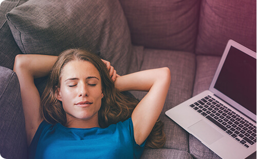 Frau liegt neben ihrem Laptop entspannt auf der Couch