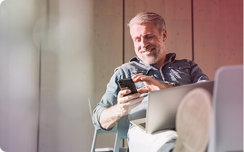 Lächelnder Mann sitzt mit Handy am Schreibtisch