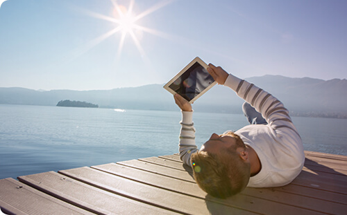 Mann auf Bootssteg liegend mit Tablet in der Hand